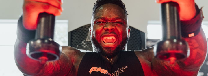 Man performing intense chest fly exercise with dumbbells under red lighting, showcasing strength and muscle engagement in a gym setting.